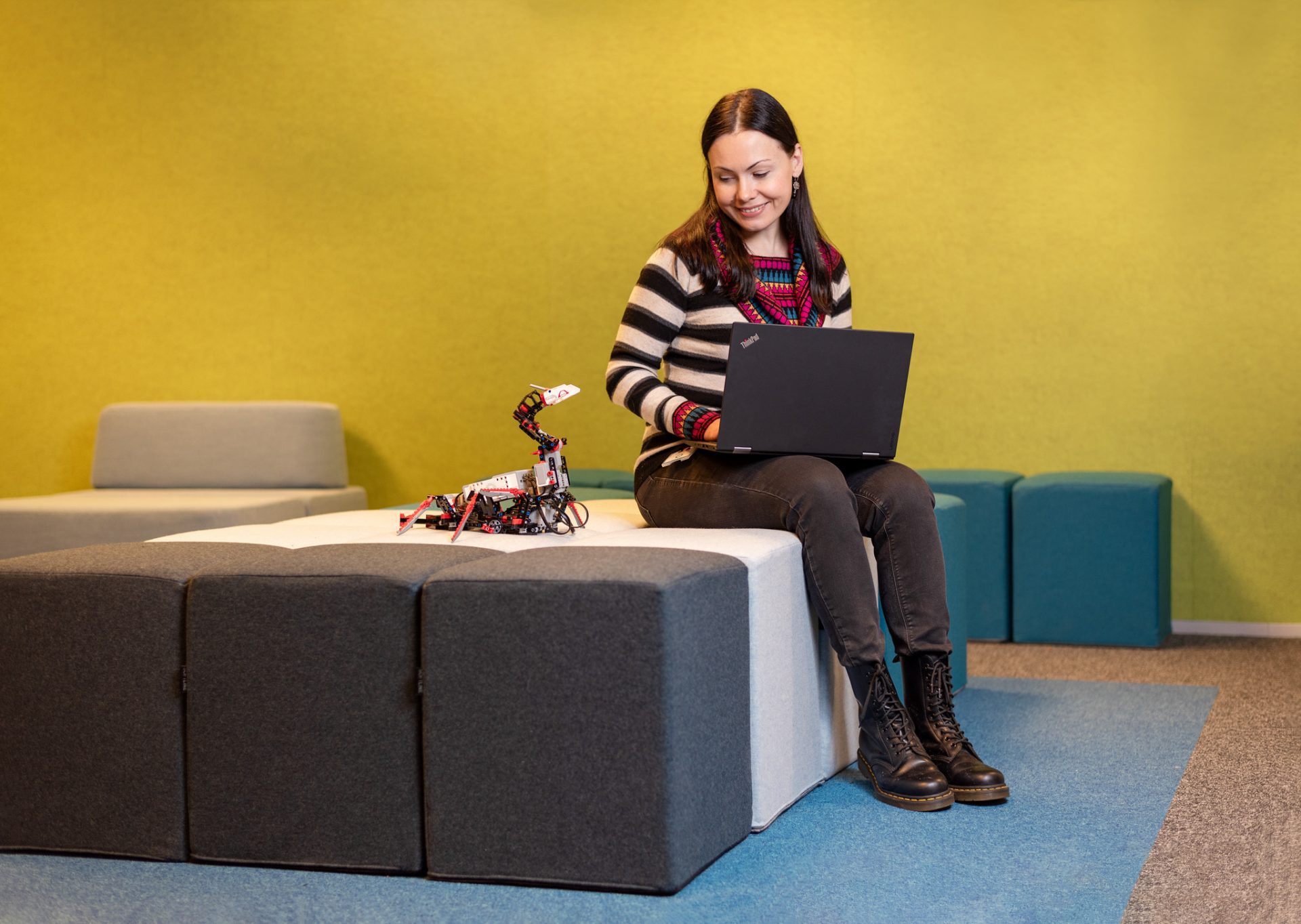 Test Engineer Karina Pietere sitting with her laptop and a toy robot.
